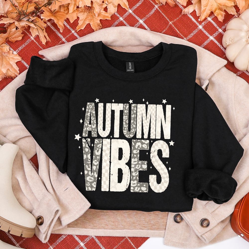 Black sweatshirt with 'AUTUMN VIBES' text on a plaid background with fall decorations.
