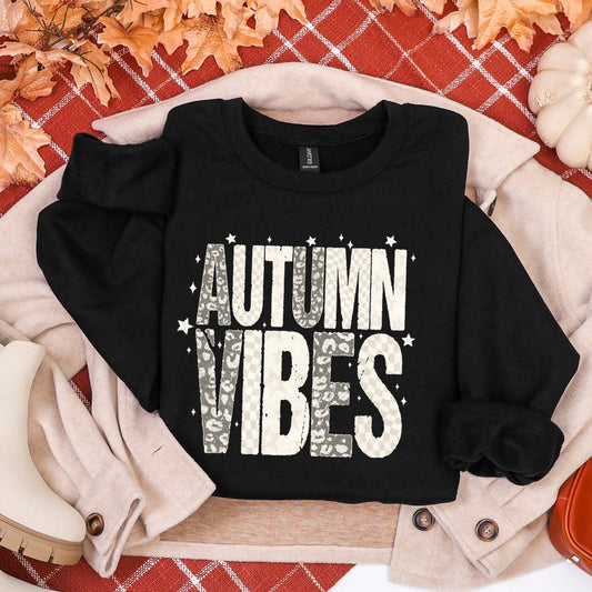 Black sweatshirt with 'AUTUMN VIBES' text on a plaid background with fall decorations.