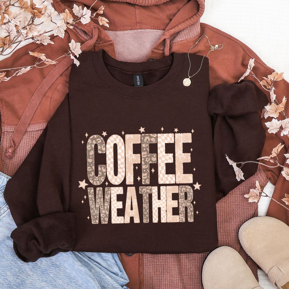 Brown sweatshirt with 'COFFEE WEATHER' text on a laid-out outfit with floral decorations.