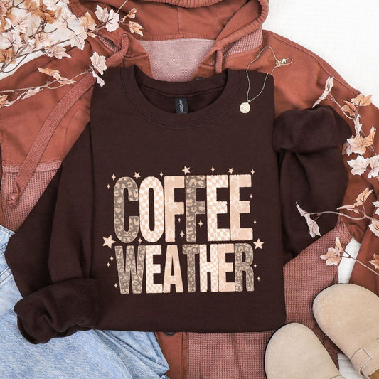 Brown sweatshirt with 'COFFEE WEATHER' text on a laid-out outfit with floral decorations.