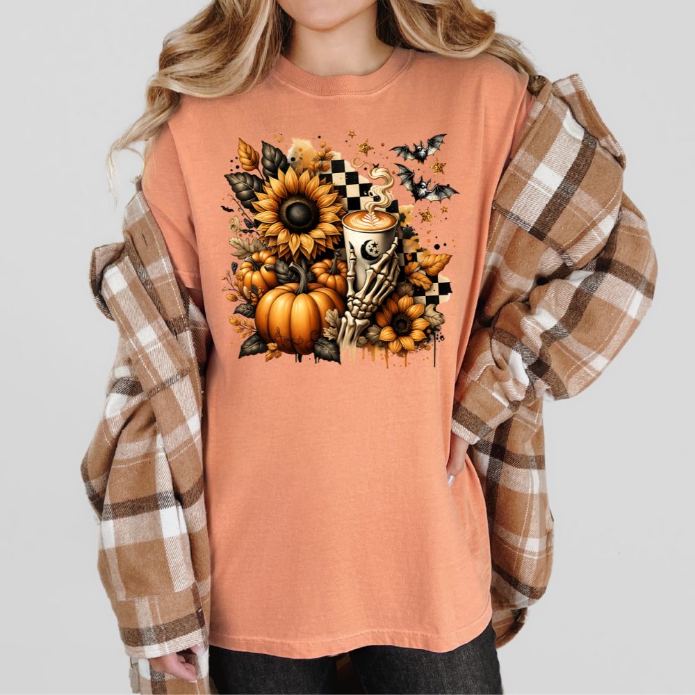 Person wearing a peach-colored shirt with Halloween-themed design, including pumpkins, sunflowers, and a skeleton hand holding a cup.