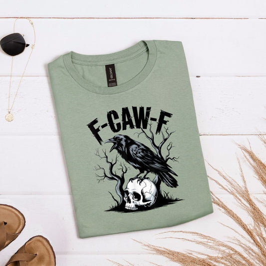 Sage green T-shirt with crow perched on skull, tree branches, and large “F-CAW-F” distressed text