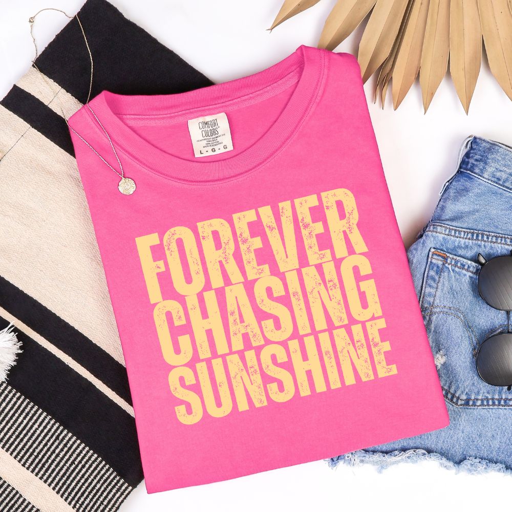 Comfort Colors Neon pink t-shirt folded with “Forever Chasing Sunshine” in distressed yellow lettering.