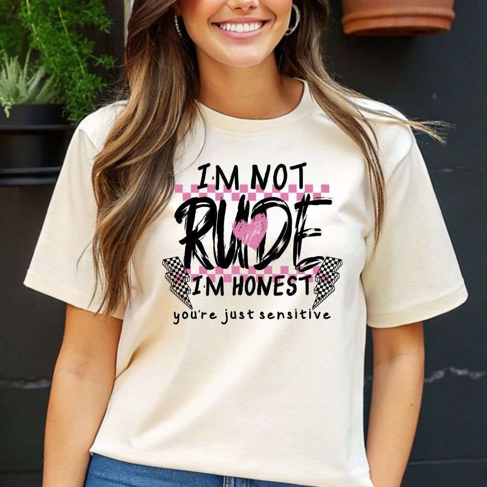 Cream colors graphic t-shirt featuring the phrase “I'm Not Rude I'm Honest You're Just Sensitive” with pink heart and checkered accents.