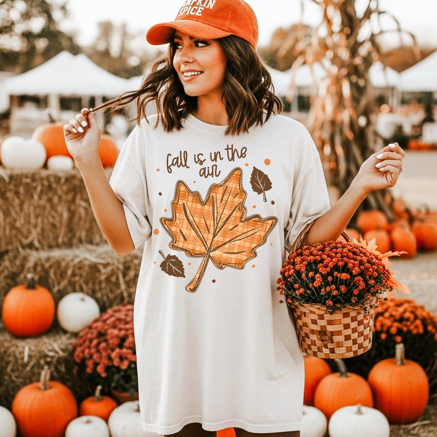 Woman wearing an ivory Fall Is in the Air Graphic T-Shirt with a large orange plaid maple leaf at a pumpkin patch