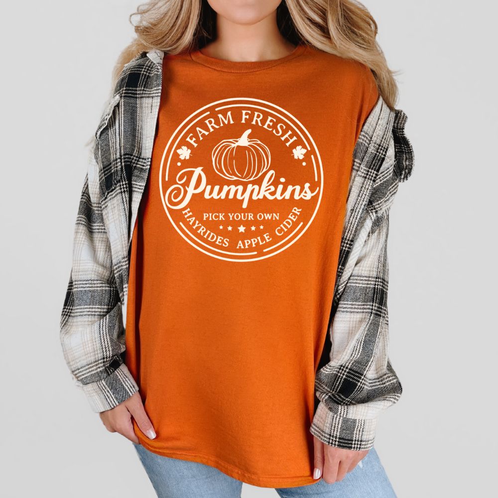 Person wearing an orange t-shirt with 'Farm Fresh Pumpkins' text and plaid shirt over shoulders.