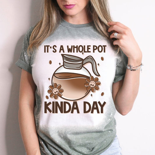 Woman wearing a green bleached T-shirt with a cartoon coffee pot and text that reads “It’s a Whole Pot Kinda Day,” surrounded by flowers and coffee beans.