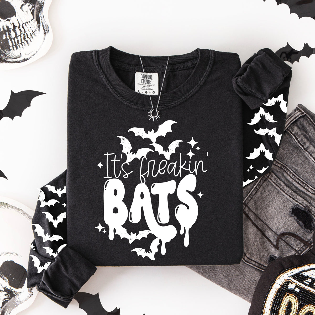 Flat lay of a black long-sleeve shirt featuring the words "It’s freakin’ BATS" with white bats and matching bat graphics down both sleeves.