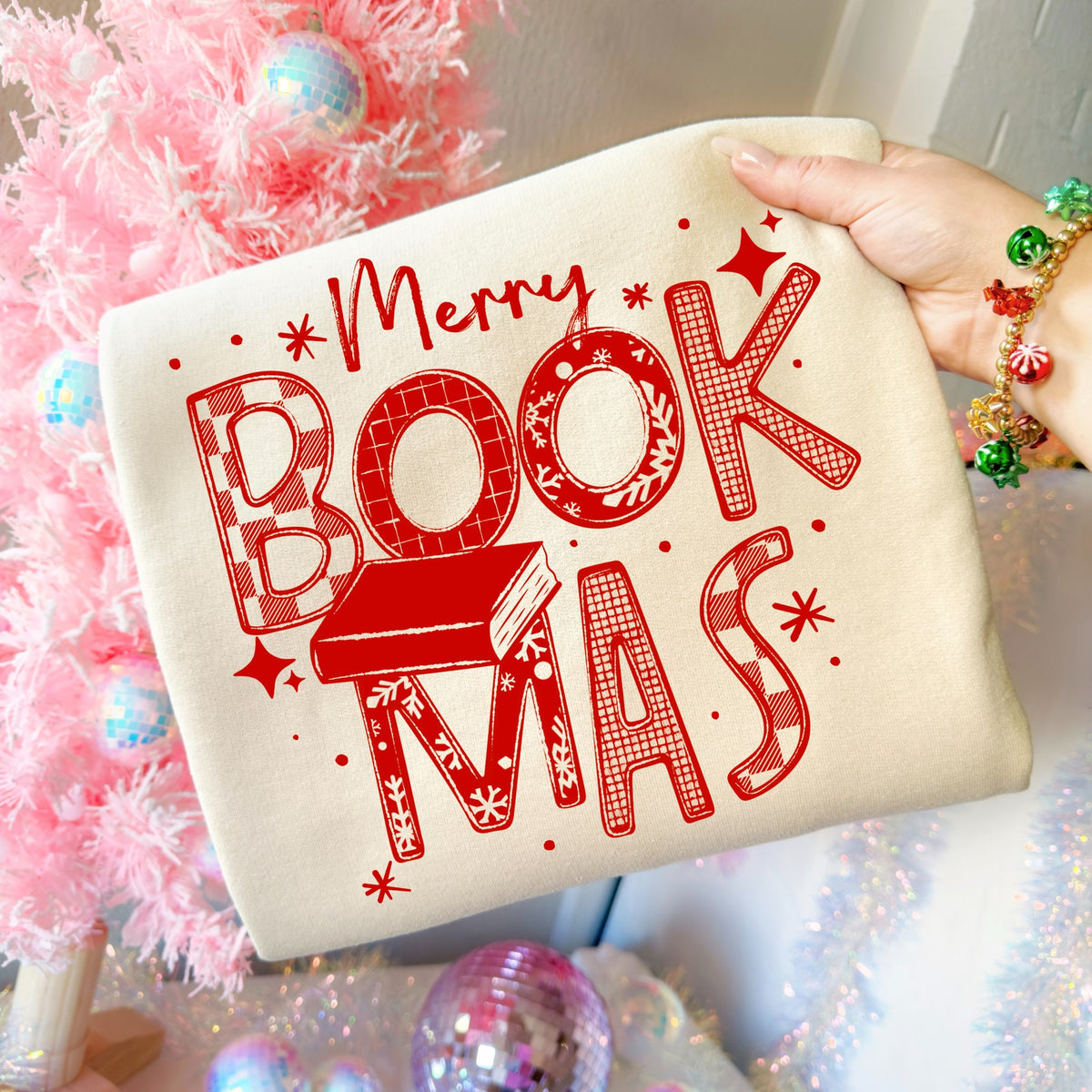Merry Bookmas Christmas book lover graphic shirt design in red on a light cream garment