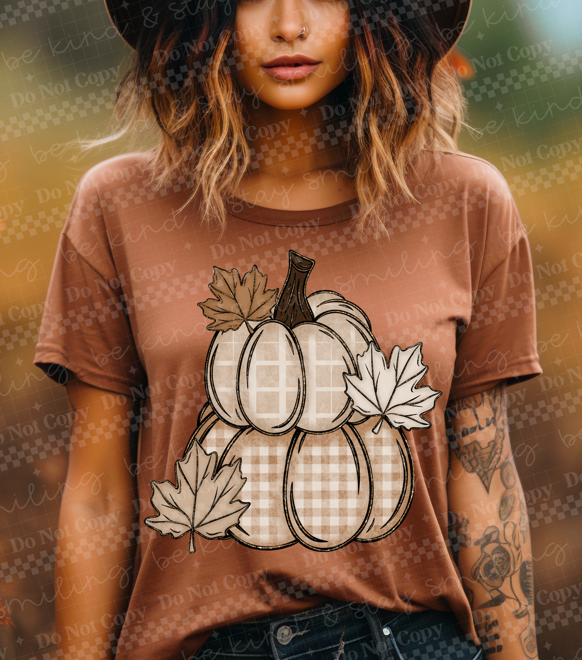 Woman wearing a rust-orange T-shirt with a neutral plaid pumpkin stack and autumn leaf graphic in cream, tan, and brown.