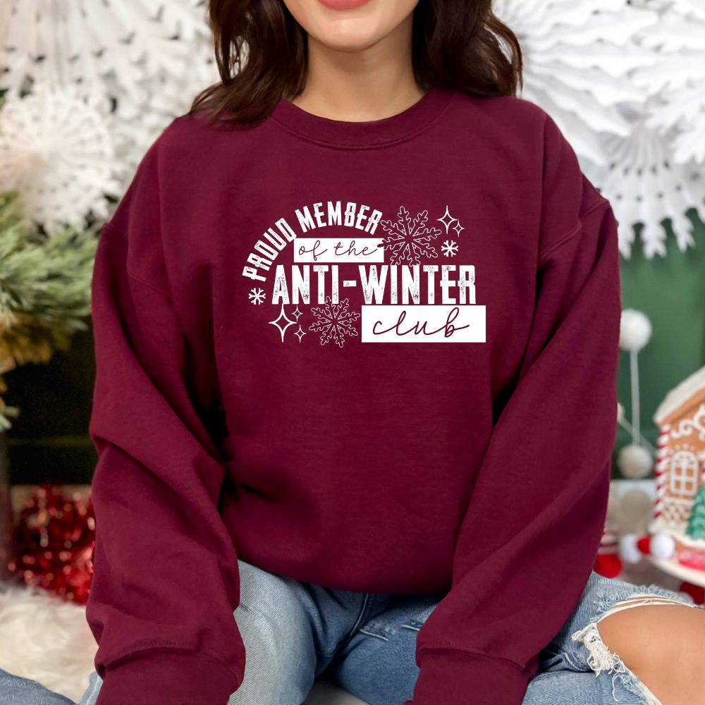 Person wearing a maroon sweatshirt with 'Proud Member of the Anti-Winter Club' text, sitting in a festive setting.