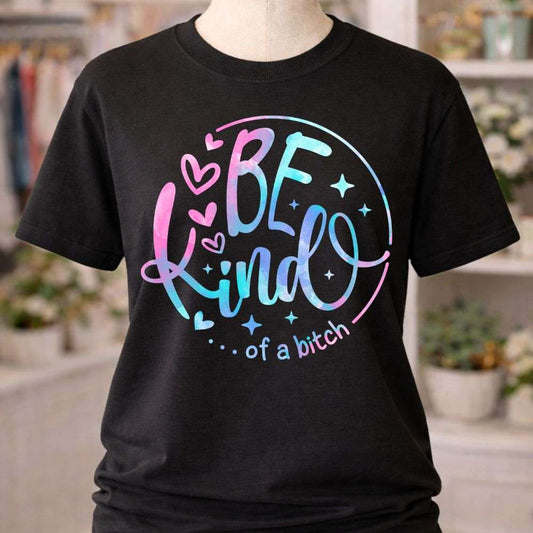 Black graphic t-shirt featuring pastel gradient text reading “Be Kind… of a Bitch” with hearts and sparkle accents.