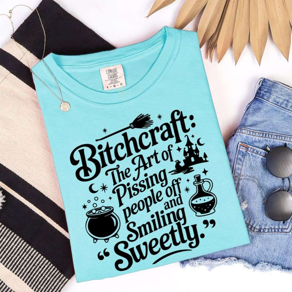 Lagoon Blue T-shirt with black graphic saying “Bitchcraft: The art of pissing people off and smiling sweetly” with witchy icons