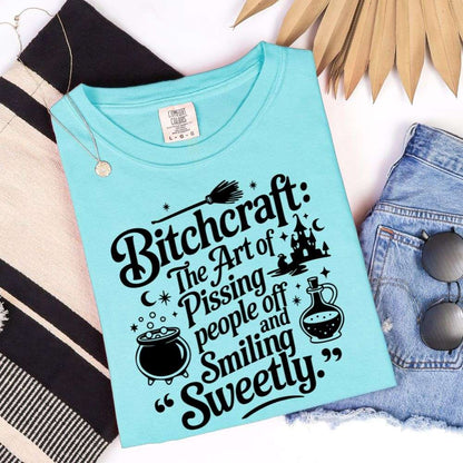 Lagoon Blue T-shirt with black graphic saying “Bitchcraft: The art of pissing people off and smiling sweetly” with witchy icons