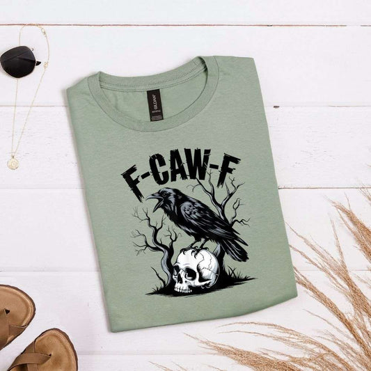 Sage green T-shirt with crow perched on skull, tree branches, and large “F-CAW-F” distressed text