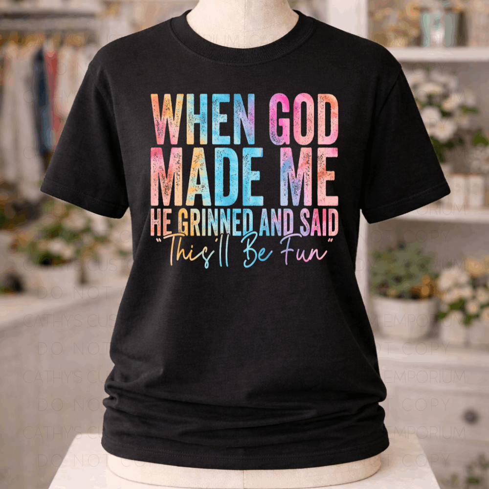 Black graphic T-shirt with colorful distressed text reading “When God Made Me He Grinned and Said This’ll Be Fun,” displayed on a mannequin.