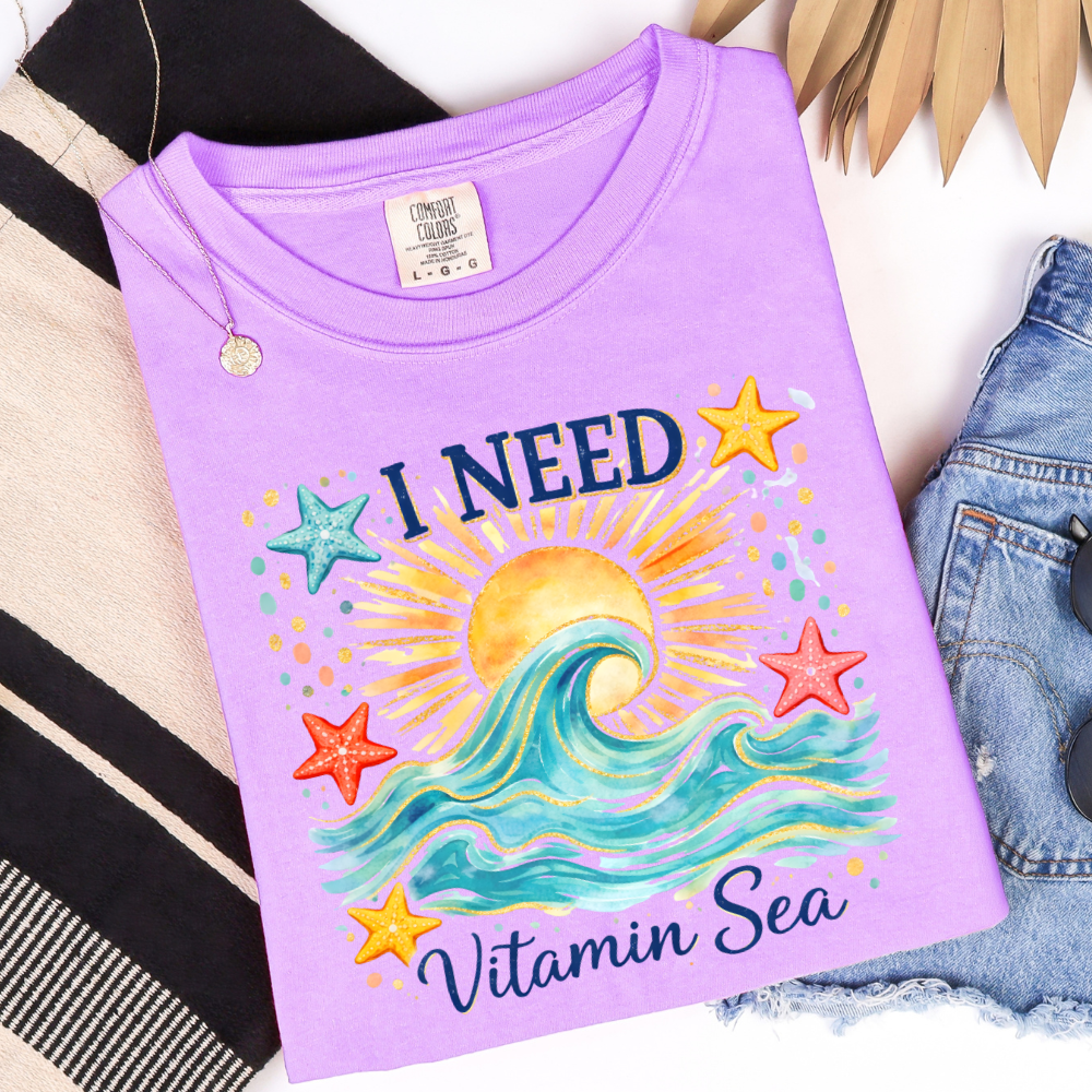 Purple t-shirt with beach-themed design and text on a white background