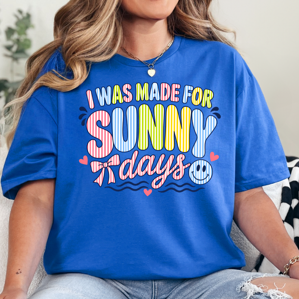 Person wearing a blue t-shirt with colorful text 'I was made for sunny days'.