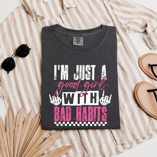 Charcoal Comfort Colors T-shirt with white and pink lettering saying “I’m just a good girl with bad habits” and skeleton hands

