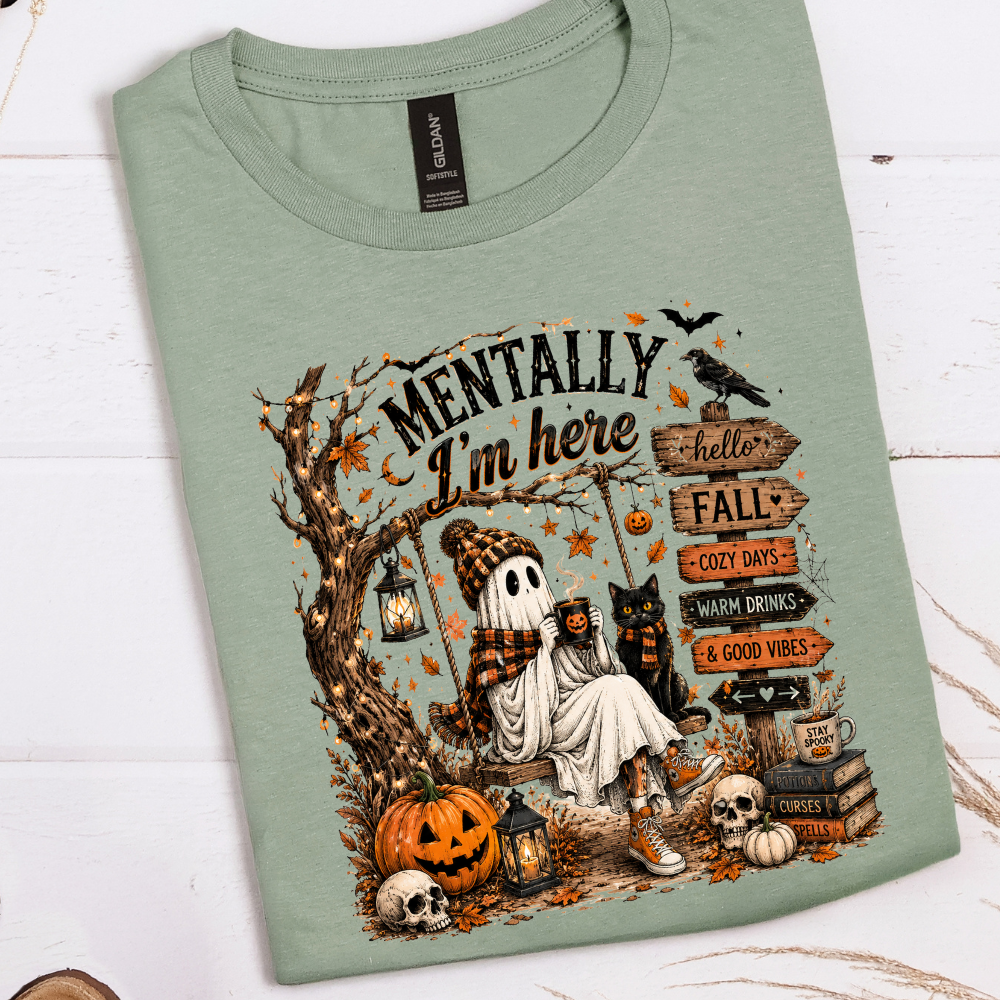 Mentally I'm Here graphic apparel shown on Gildan Softstyle Sage featuring a cozy ghost, pumpkins, black cat, lanterns, and autumn details.