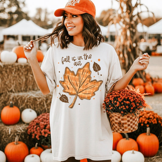 Woman wearing an ivory Fall Is in the Air Graphic T-Shirt with a large orange plaid maple leaf at a pumpkin patch