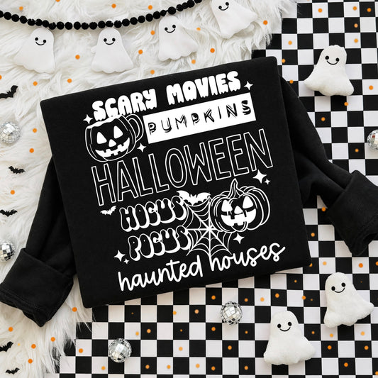 Flat lay of a black sweatshirt with a white stacked Halloween graphic featuring the words "Scary Movies," "Pumpkins," "Halloween," "Hocus Pocus," and "haunted houses" in retro fonts, with jack-o'-lanterns, spiderweb, and sparkle accents on a checkered and fur backdrop.