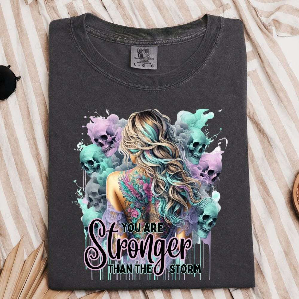 Black t-shirt with colorful graphic design and 'You are Stronger Than the Storm' text on a striped fabric background.