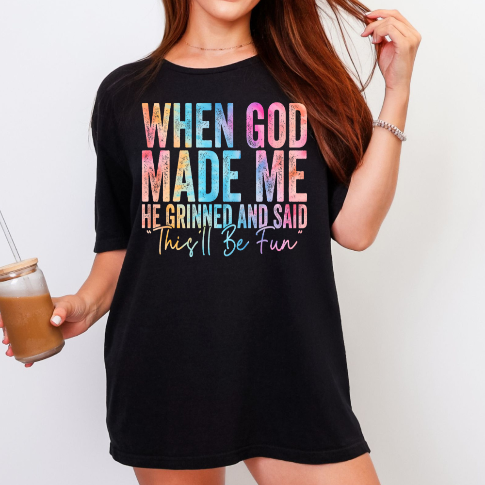 Black T-shirt with colorful “When God Made Me He Grinned and Said This’ll Be Fun” graphic.