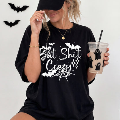 Woman wearing a black T-shirt with a white Bat Shit Crazy Halloween graphic featuring bats, spiderwebs, dots, and sparkles.