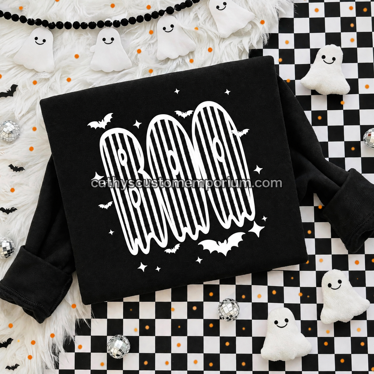 Black BOO Halloween sweatshirt with white striped ghost lettering and bat accents on a checkered flat lay