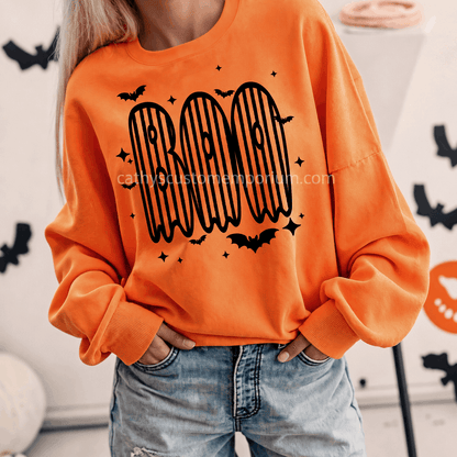 Woman wearing an orange BOO Halloween sweatshirt with black striped ghost lettering and bat accents