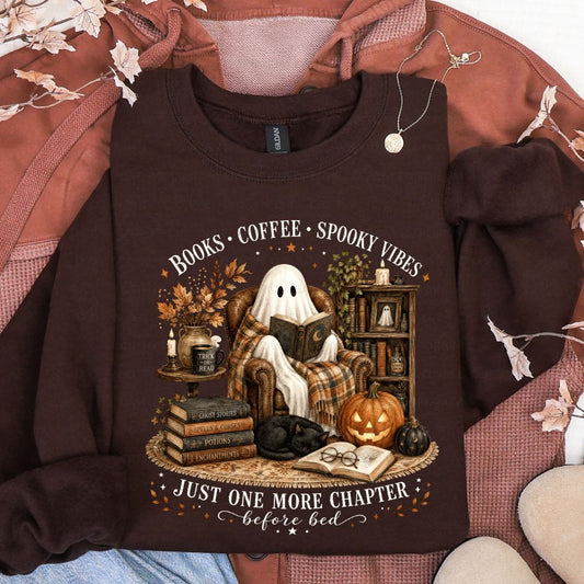 Dark brown sweatshirt featuring a ghost reading in a cozy Halloween library scene with pumpkins, books, coffee, and the words Books Coffee Spooky Vibes and Just One More Chapter Before Bed.