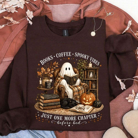 Dark brown sweatshirt featuring a ghost reading in a cozy Halloween library scene with pumpkins, books, coffee, and the words Books Coffee Spooky Vibes and Just One More Chapter Before Bed.