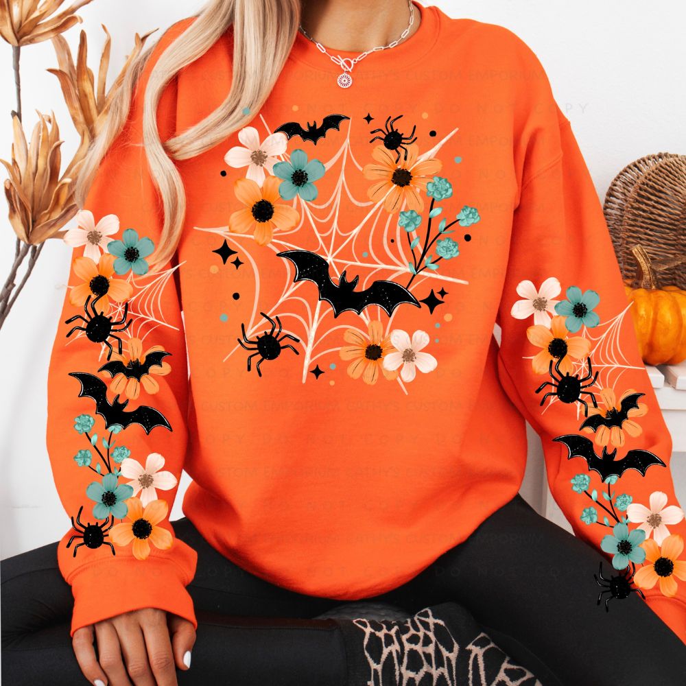 Bright orange sweatshirt with orange, cream, and teal flowers, white spiderwebs, black bats and spiders across the front and sleeves.