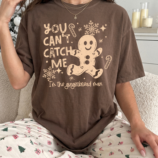 Funny You Can't Catch Me gingerbread man Christmas graphic shown on a dark brown T-shirt