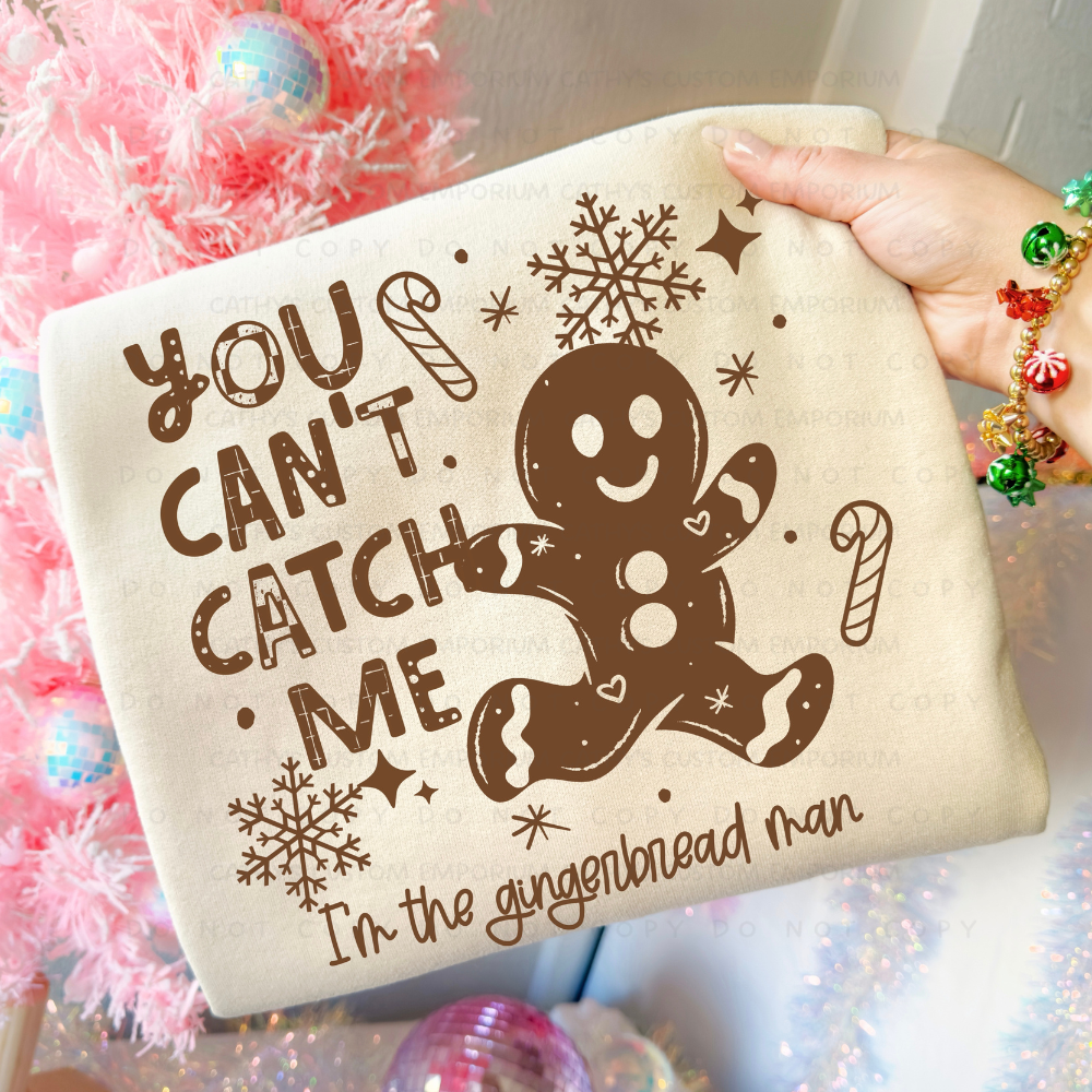 Funny You Can't Catch Me gingerbread man Christmas graphic shown on a light cream sweatshirt