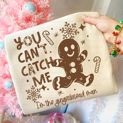 Funny You Can't Catch Me gingerbread man Christmas graphic shown on a light cream sweatshirt