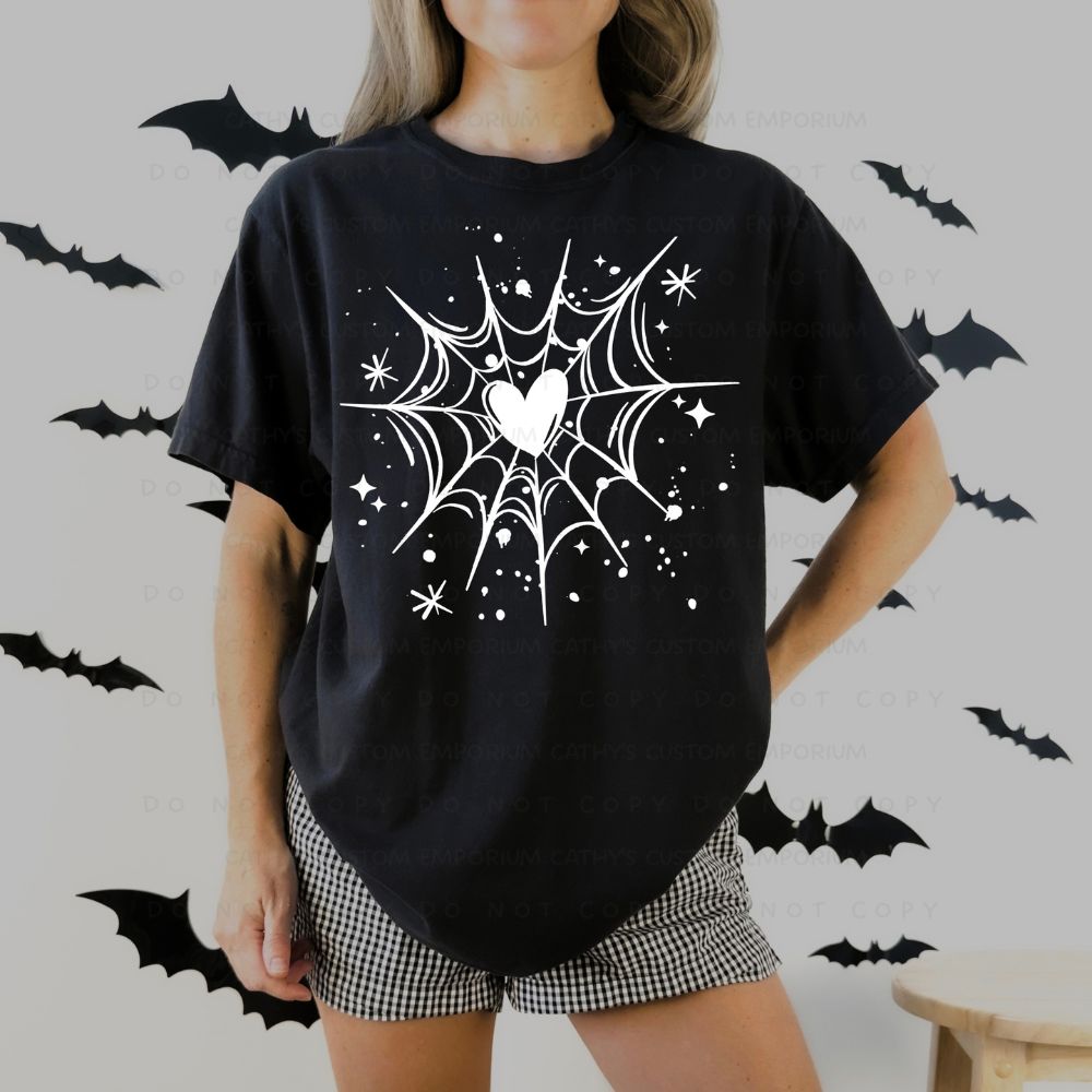 Black T-shirt with a white spiderweb graphic centered around a heart, surrounded by stars and paint-splatter accents.