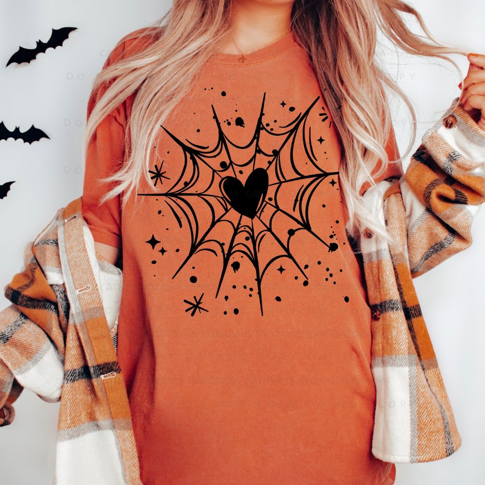 Rust-orange T-shirt with a black spiderweb graphic centered around a heart, surrounded by stars and paint-splatter accents.