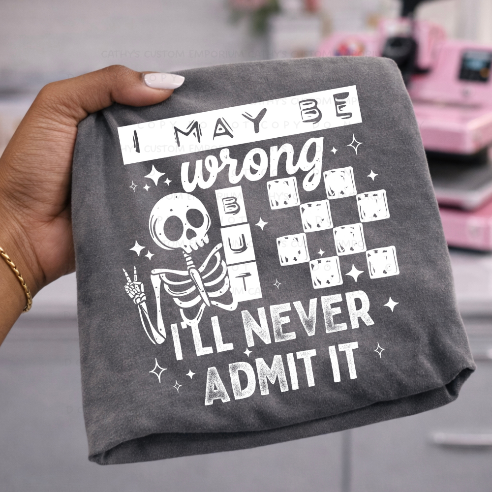 Dark gray shirt featuring a skeleton and crossword-style design reading I May Be Wrong But I'll Never Admit It in white.