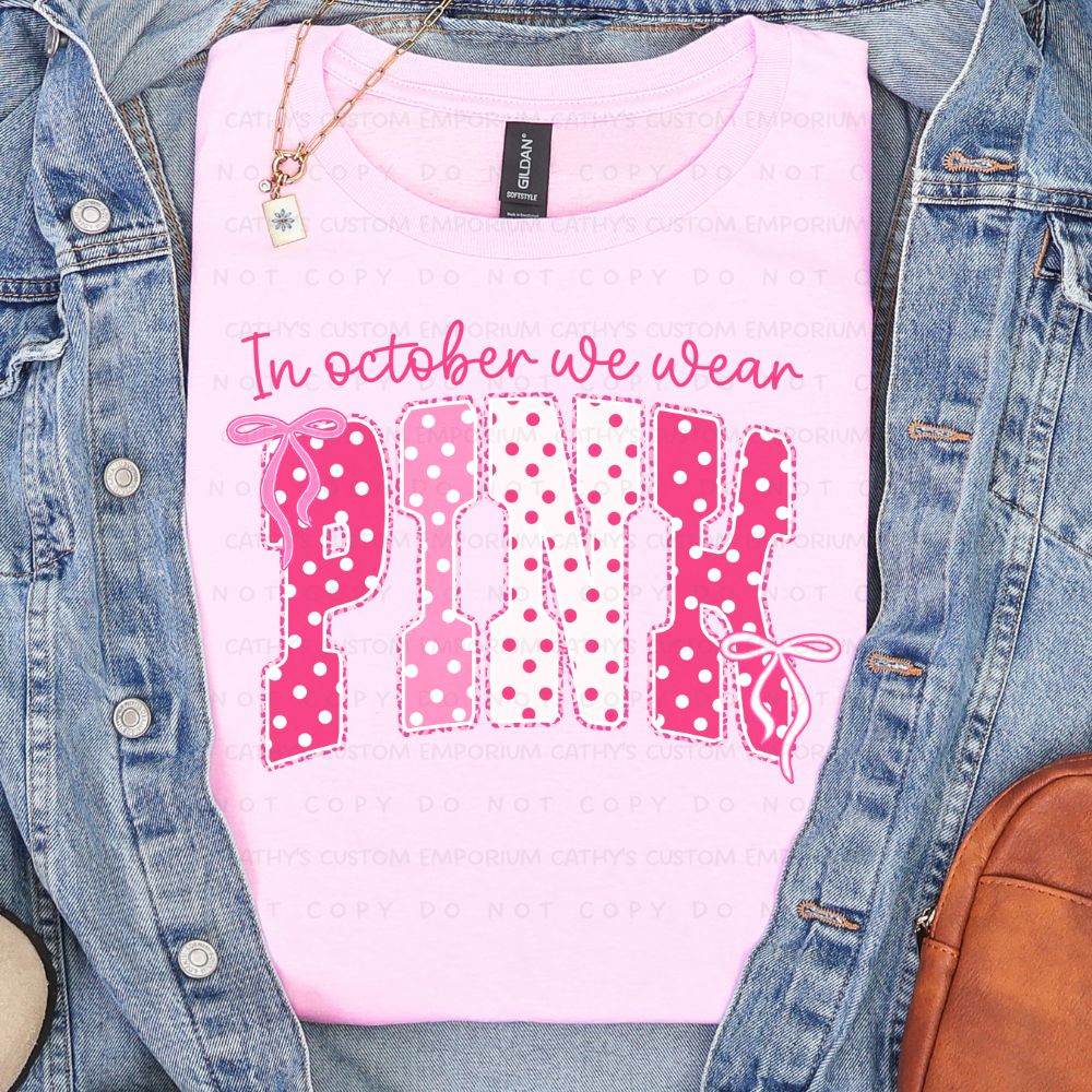 Light pink shirt featuring the phrase In October We Wear Pink in pink and white polka-dot lettering with bow accents.
