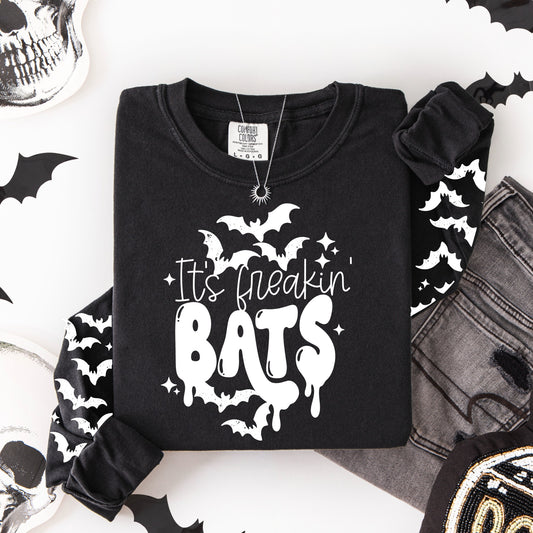 Flat lay of a black long-sleeve shirt featuring the words "It’s freakin’ BATS" with white bats and matching bat graphics down both sleeves.