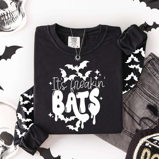 Flat lay of a black long-sleeve shirt featuring the words "It’s freakin’ BATS" with white bats and matching bat graphics down both sleeves.