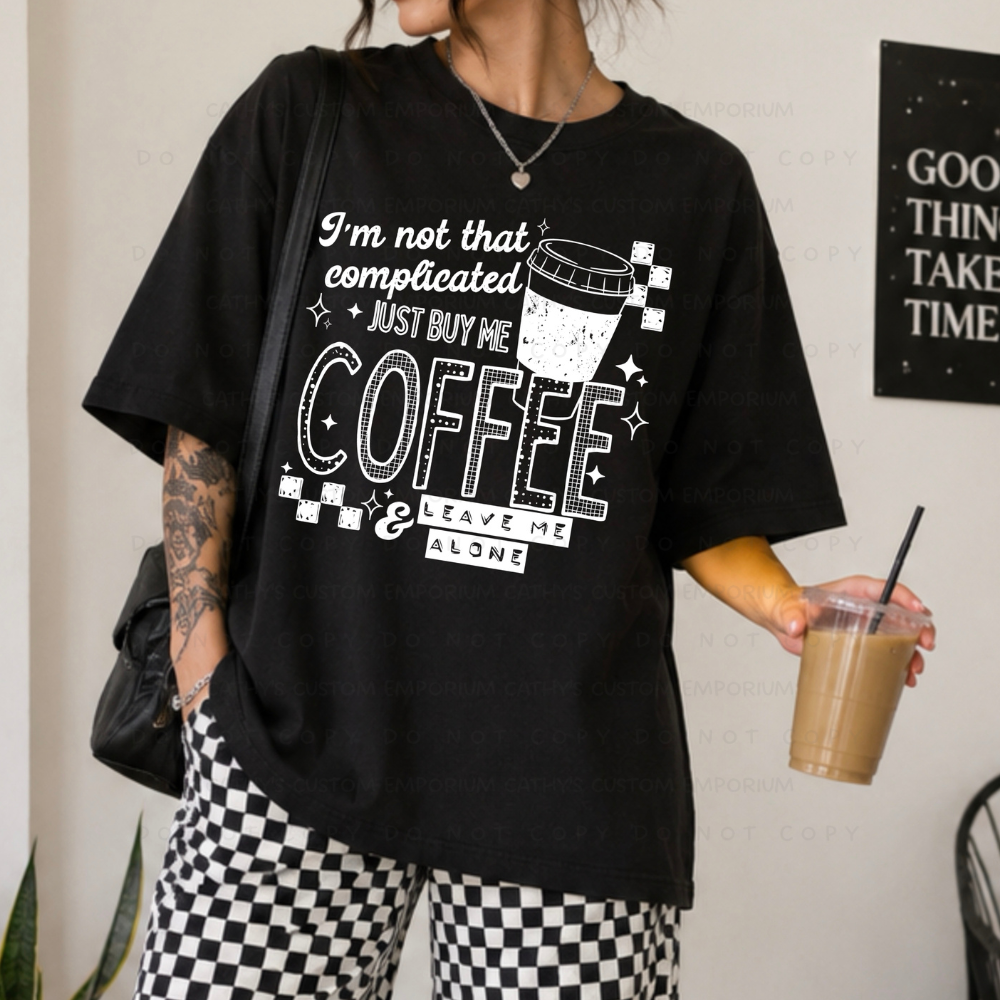 Black shirt featuring a white graphic that reads I'm Not That Complicated, Just Buy Me Coffee and Leave Me Alone with a coffee cup and checkerboard accents.