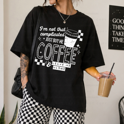 Black shirt featuring a white graphic that reads I'm Not That Complicated, Just Buy Me Coffee and Leave Me Alone with a coffee cup and checkerboard accents.