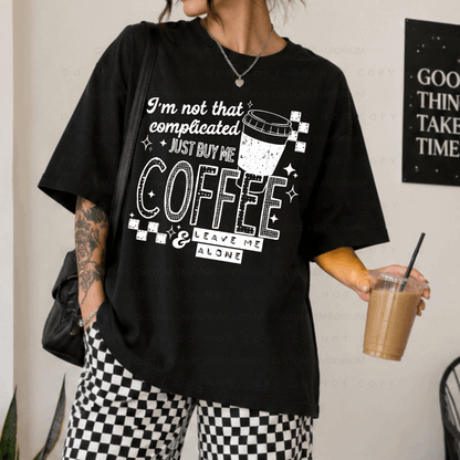 Black shirt featuring a white graphic that reads I'm Not That Complicated, Just Buy Me Coffee and Leave Me Alone with a coffee cup and checkerboard accents.