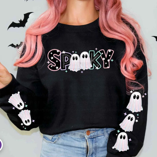 Woman with pink hair wearing a black Spooky Halloween sweatshirt with pastel ghost lettering, sparkles, and coordinating ghost sleeve designs