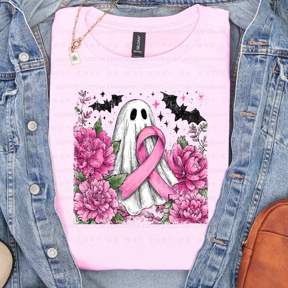 Light pink shirt featuring a white ghost holding a pink breast cancer ribbon surrounded by pink flowers, greenery, bats, and stars.
