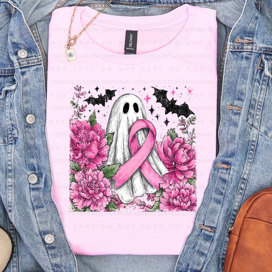 Light pink shirt featuring a white ghost holding a pink breast cancer ribbon surrounded by pink flowers, greenery, bats, and stars.