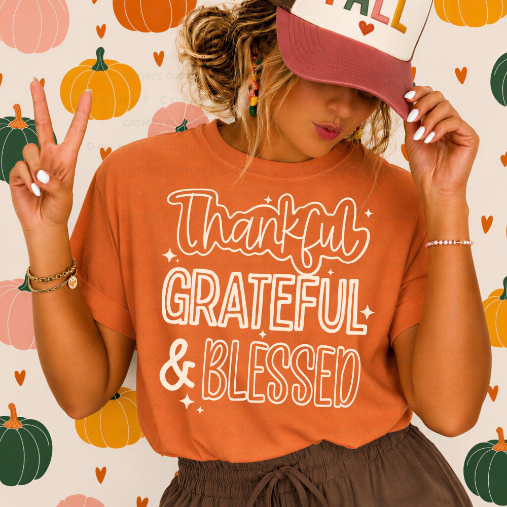 Woman wearing an orange Thanksgiving graphic T-shirt with white Thankful Grateful and Blessed lettering against a colorful pumpkin background.